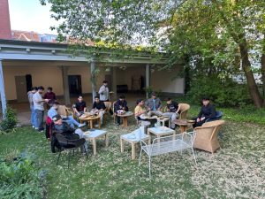 Jugendliche sitzen in einem Garten in kleinen Gruppen zusammen, sprechen und essen gemeinsam. Die Szene zeigt ein Treffen des Projekts „Big Point“ der GWA St. Pauli für bildungsbenachteiligte junge Menschen.