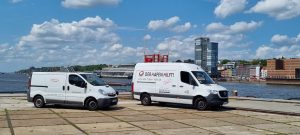 Zwei Transporter des Vereins „Der Hafen Hilft!“ stehen am Hamburger Hafen vor der Skyline; sie symbolisieren die Sachspendenlogistik und Einsatzfahrten des Spendenschippers.